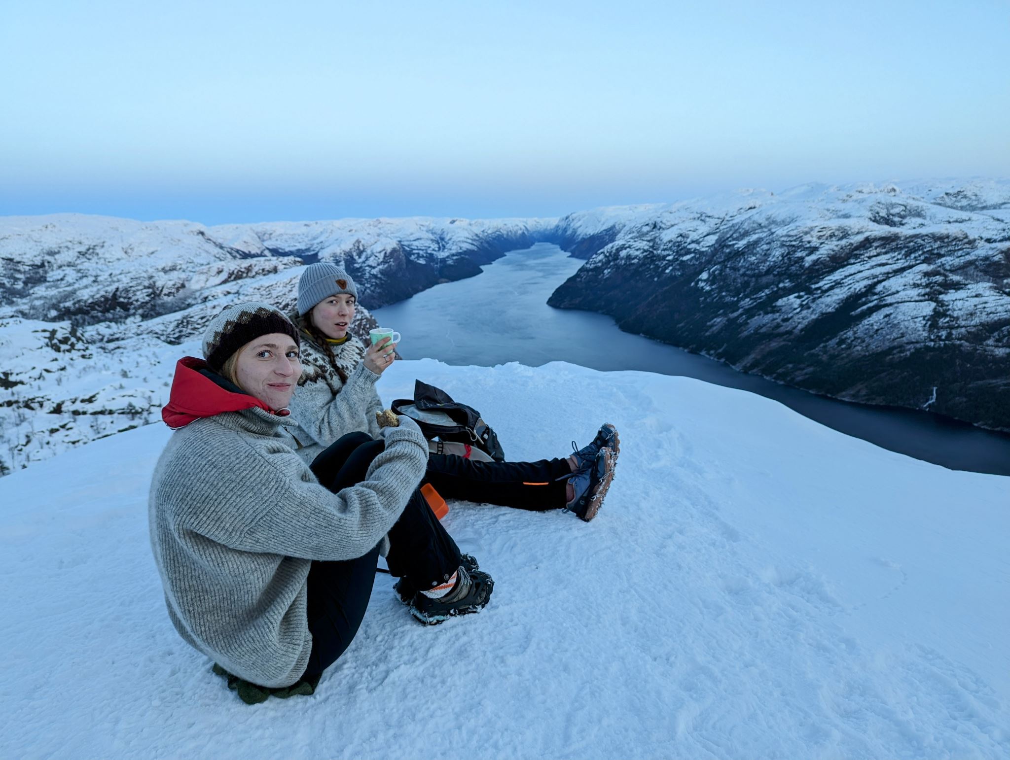 2 young women sitting on pulpit rock norway wintertime hiking